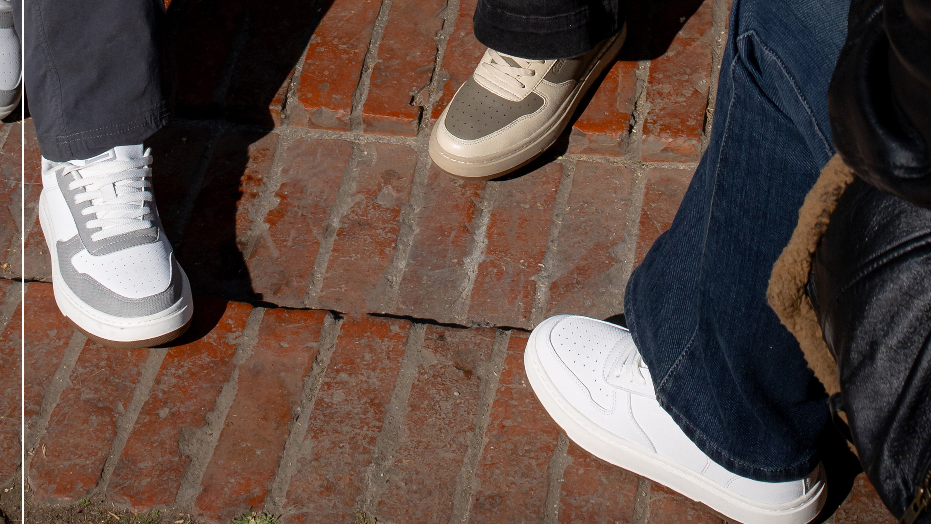 Two pairs of feet wearing sneakers on a brick sidewalk.